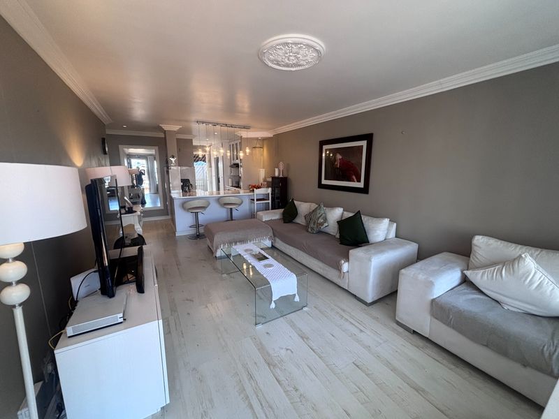 Spacious open-plan living area featuring a kitchen island with breakfast bar, elegant crown molding, ceiling rose, and light-toned laminate flooring.