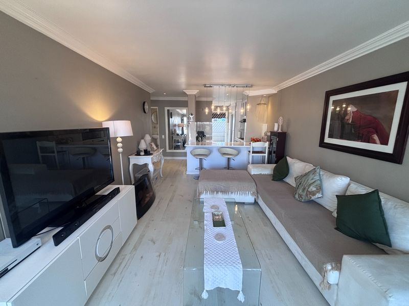 Open-plan living area featuring light-toned laminate flooring, crown molding, and a kitchen island with pendant lighting, creating a cohesive and functional living space.