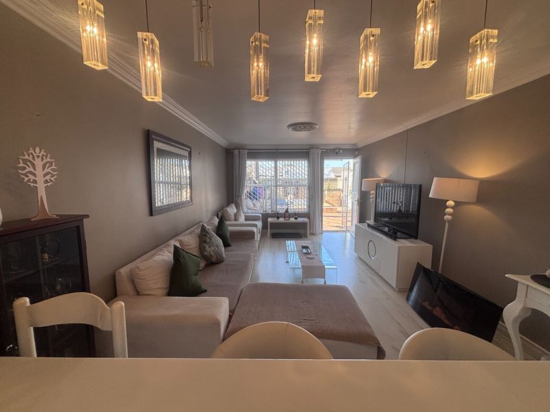 A well-lit living room featuring modern pendant lighting, laminate flooring, and direct access to an outdoor patio area through a secure sliding door.