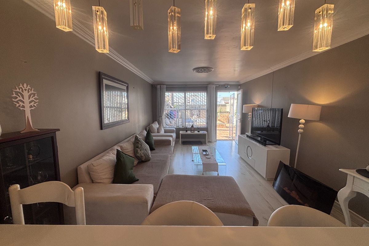 A well-lit living room featuring modern pendant lighting, laminate flooring, and direct access to an outdoor patio area through a secure sliding door.