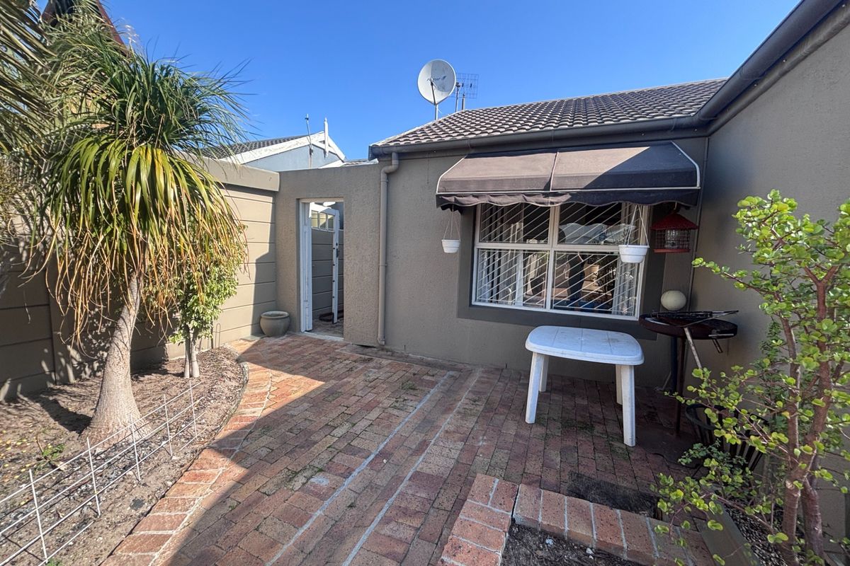 A rear courtyard area featuring brick paving, a window awning with security bars, and a boundary wall.