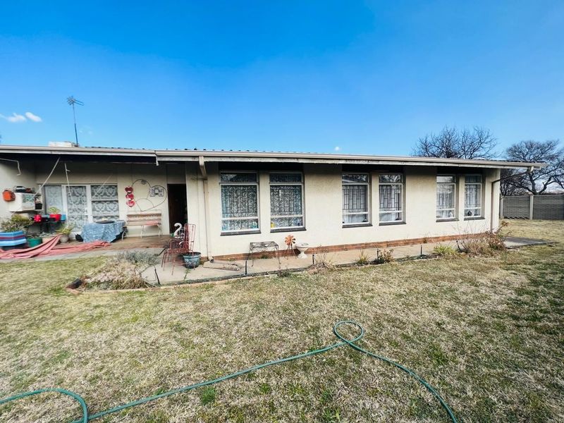 Rear view of the house featuring a covered patio area, concrete paving, and a large garden space with established lawn.