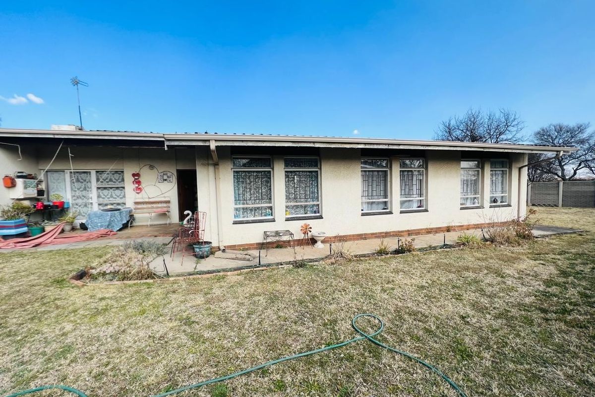 Rear view of the house featuring a covered patio area, concrete paving, and a large garden space with established lawn.