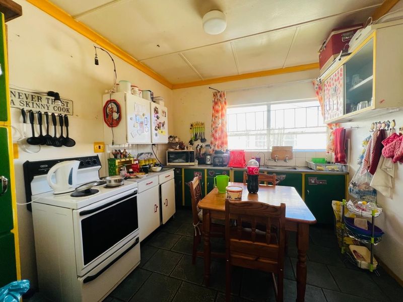 A dated kitchen featuring built-in cabinetry, a stainless steel sink, and a freestanding stove, with tiled flooring and a window with security bars.