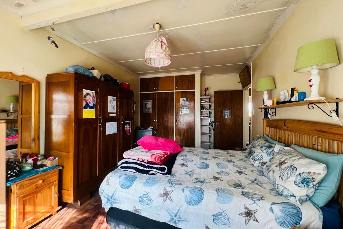 A bedroom featuring built-in wooden cupboards and parquet flooring, requiring cosmetic updates to the ceiling and wall finishes.