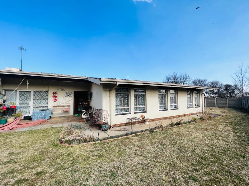 Rear view of the house featuring a paved patio area, aluminum window frames, and a surrounding garden with a concrete boundary wall.