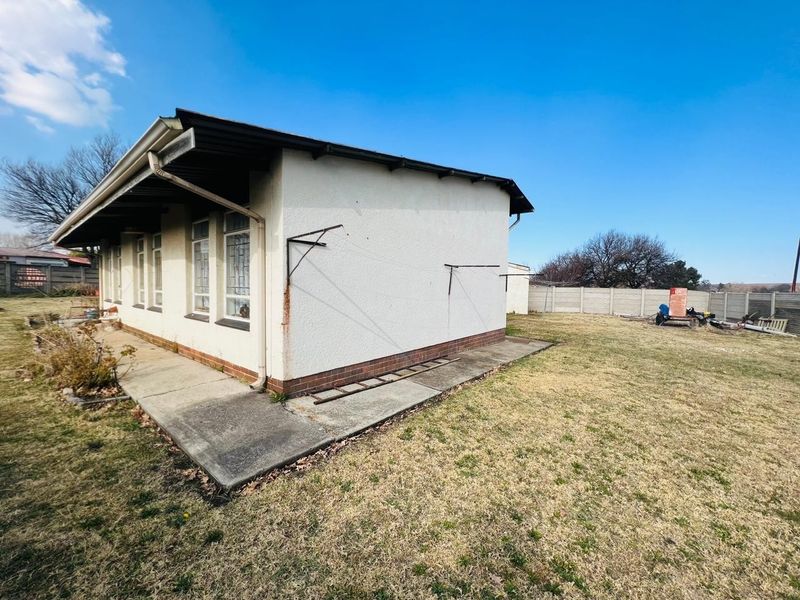 Rear view of the property showing a concrete apron, exterior wall with metal washing line brackets, and a surrounding precast concrete boundary wall.