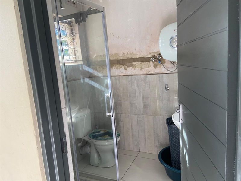 A compact bathroom featuring a shower enclosure, toilet, and wall-mounted water heater, currently requiring finishing work on the wall surfaces.