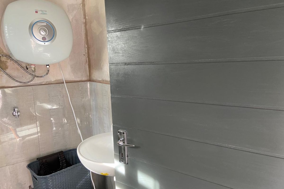 A small bathroom space featuring a wall-mounted basin and electric water heater, currently requiring wall finishing and cosmetic updates.