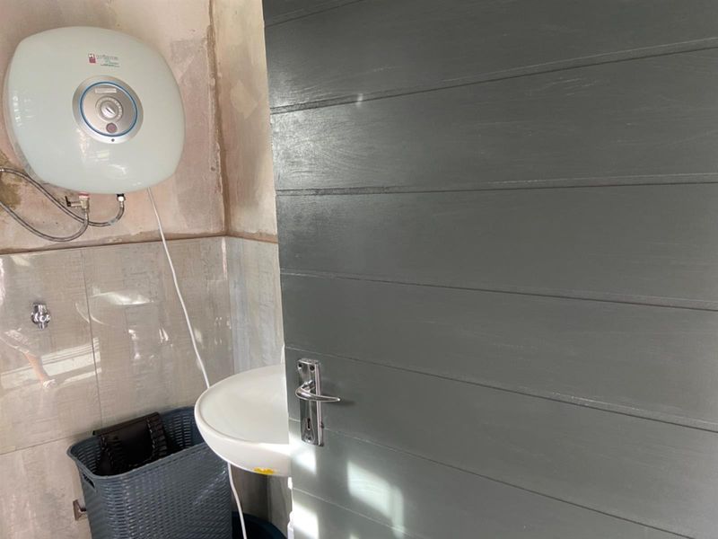 A small bathroom space featuring a wall-mounted basin and electric water heater, currently requiring wall finishing and cosmetic updates.