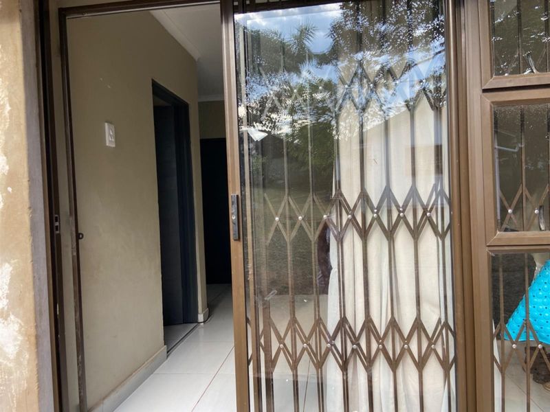 A covered patio area featuring tiled flooring, a sliding glass door, and a security gate, providing access to the interior of the cottage.