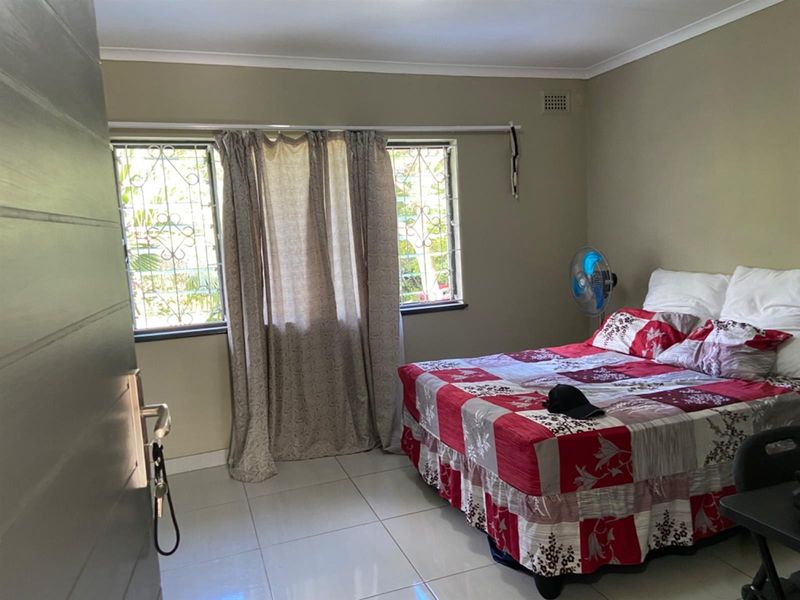 A bedroom featuring tiled flooring, security bars on the windows, and a ventilation grille, providing a functional and secure living space.
