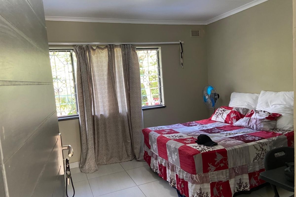A functional bedroom featuring tiled flooring, security bars on the windows, and neutral wall finishes.