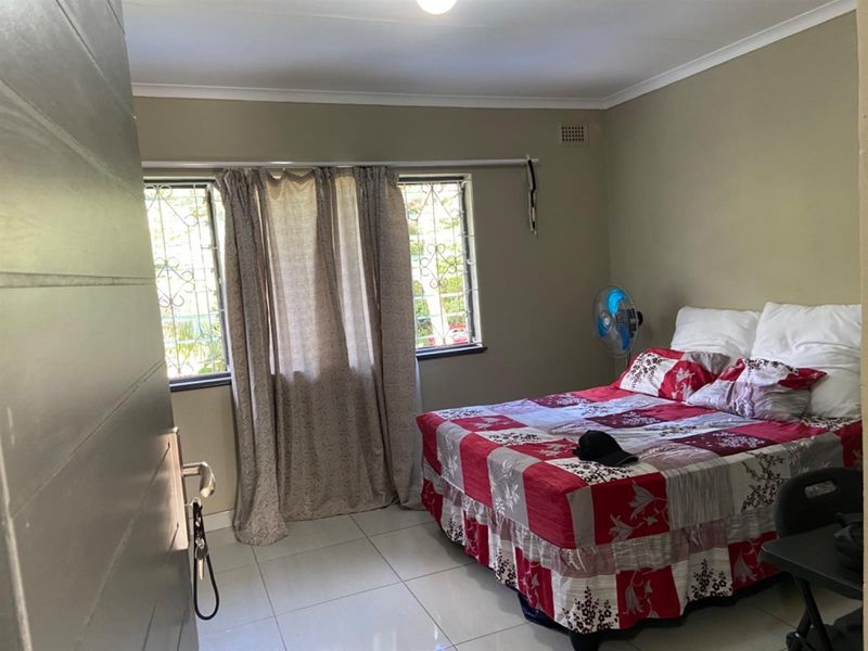 A functional bedroom featuring tiled flooring, security bars on the windows, and neutral wall finishes.