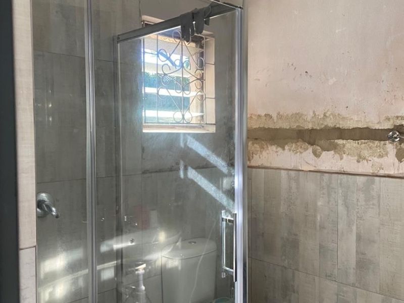 A bathroom in the process of renovation, featuring a glass shower enclosure, toilet, and partially tiled walls requiring finishing touches.