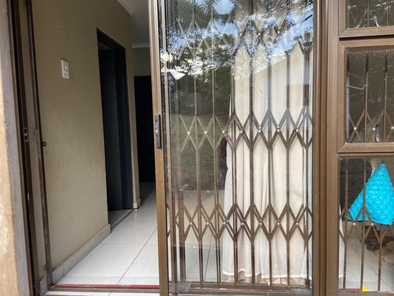 A covered patio area featuring tiled flooring, a sliding glass door, and a fitted security gate.