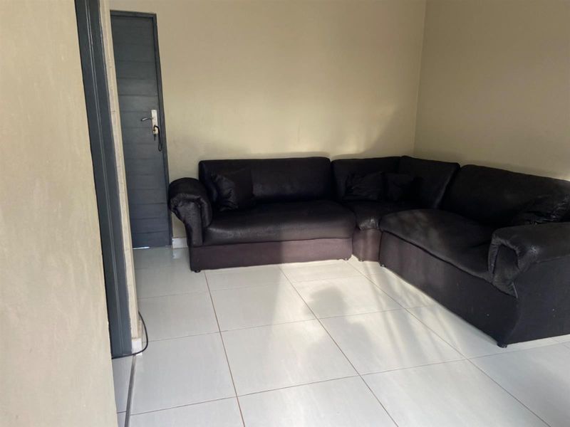 A simple living room area featuring light-colored floor tiles and a neutral wall finish.