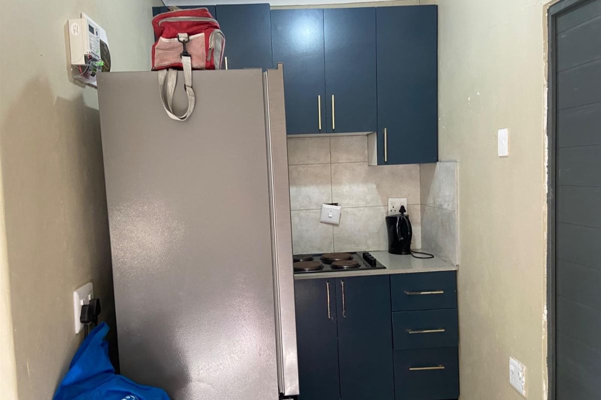 Compact kitchen area featuring dark blue cabinetry, a built-in electric hob, and tiled splashback, providing essential cooking functionality in a small footprint.