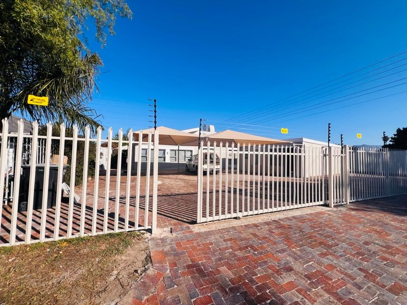 Front view of the property featuring a secure steel gate, paved driveway, and a shade sail carport structure.