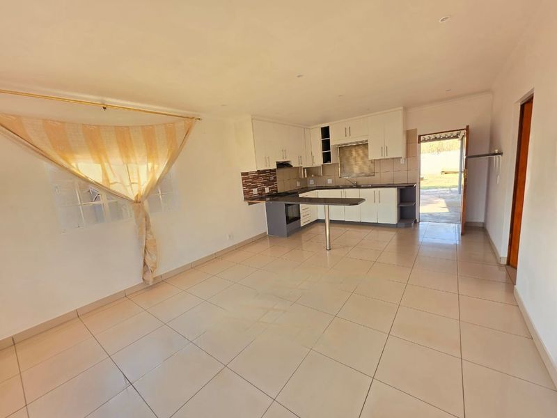 Open plan living and kitchen area featuring tiled flooring, built-in cabinetry, and a breakfast bar with direct access to the rear exterior.