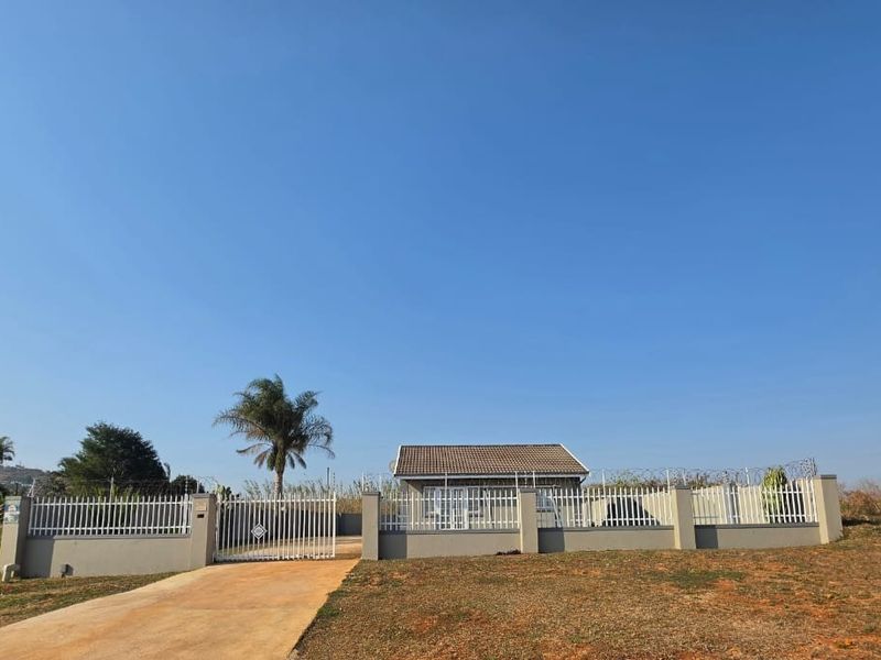 Front view of a residential property featuring a secure perimeter wall with metal gates, razor wire, and a concrete driveway leading to the house.