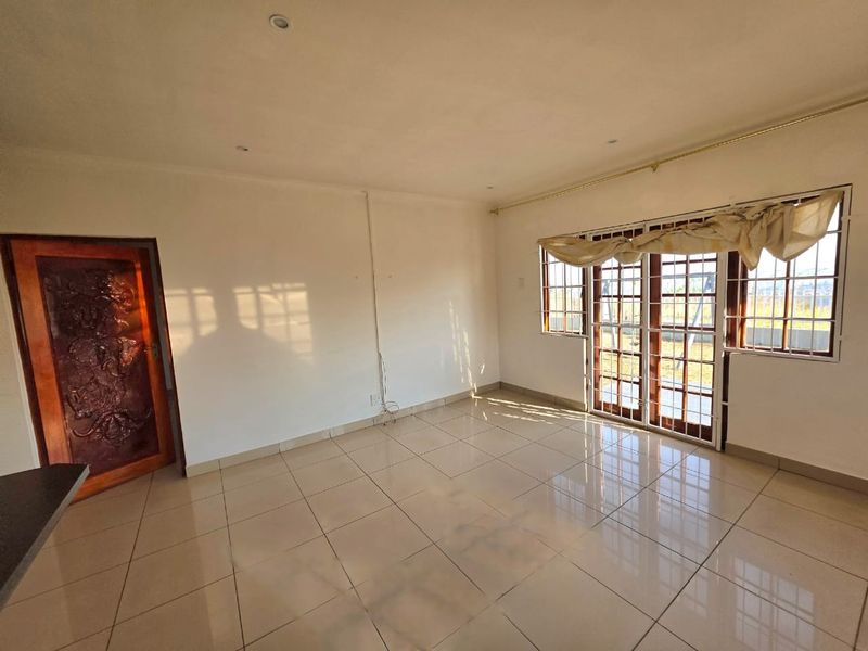 A bright, empty living room featuring large tiled floors, recessed lighting, and wooden framed glass doors leading to the exterior.