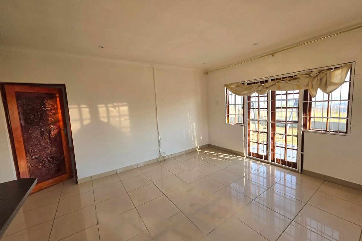 A bright, empty living room featuring large tiled floors, recessed lighting, and wooden framed glass doors leading to the exterior.
