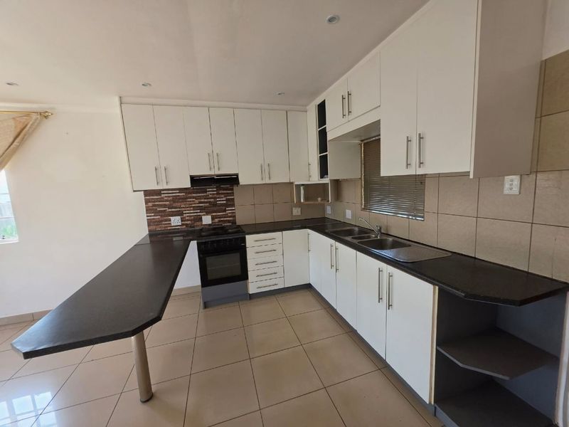 A clean, functional kitchen featuring white cabinetry, dark granite countertops, a breakfast nook, and built-in appliances with neutral tiled flooring.