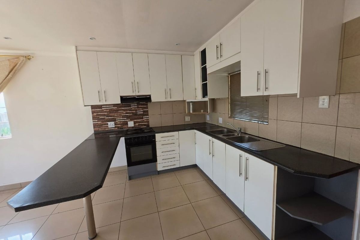 A clean, functional kitchen featuring white cabinetry, dark granite countertops, a breakfast nook, and built-in appliances with neutral tiled flooring.