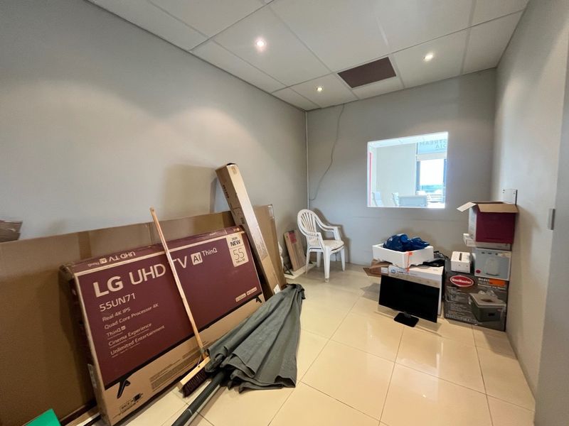 A vacant office space featuring tiled flooring, a suspended ceiling with recessed lighting, and an internal window looking into an adjacent area.