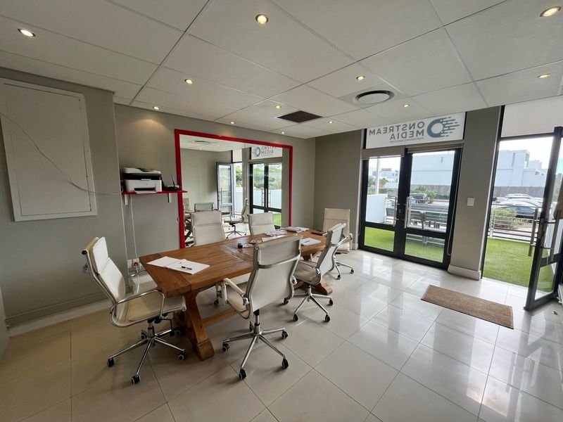 A modern office space featuring polished floor tiles, a suspended ceiling with recessed lighting, and direct access to an outdoor patio area.