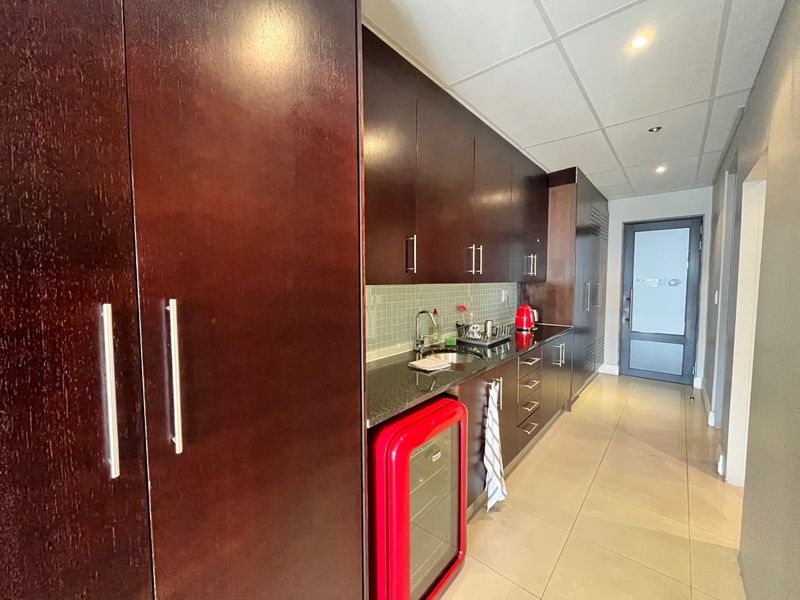 A functional office kitchenette featuring dark wood cabinetry, granite countertops, a tiled backsplash, and modern tiled flooring.