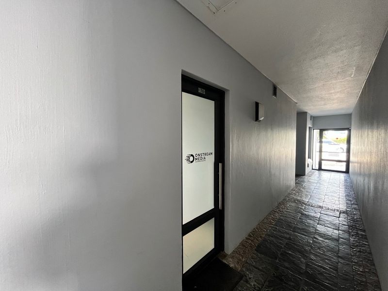 A clean, well-lit office hallway featuring stone tile flooring and a modern glass-paneled entrance door.