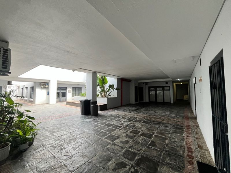 A covered outdoor patio area featuring durable tiled flooring, recessed lighting, and an integrated air conditioning unit within an office complex setting.
