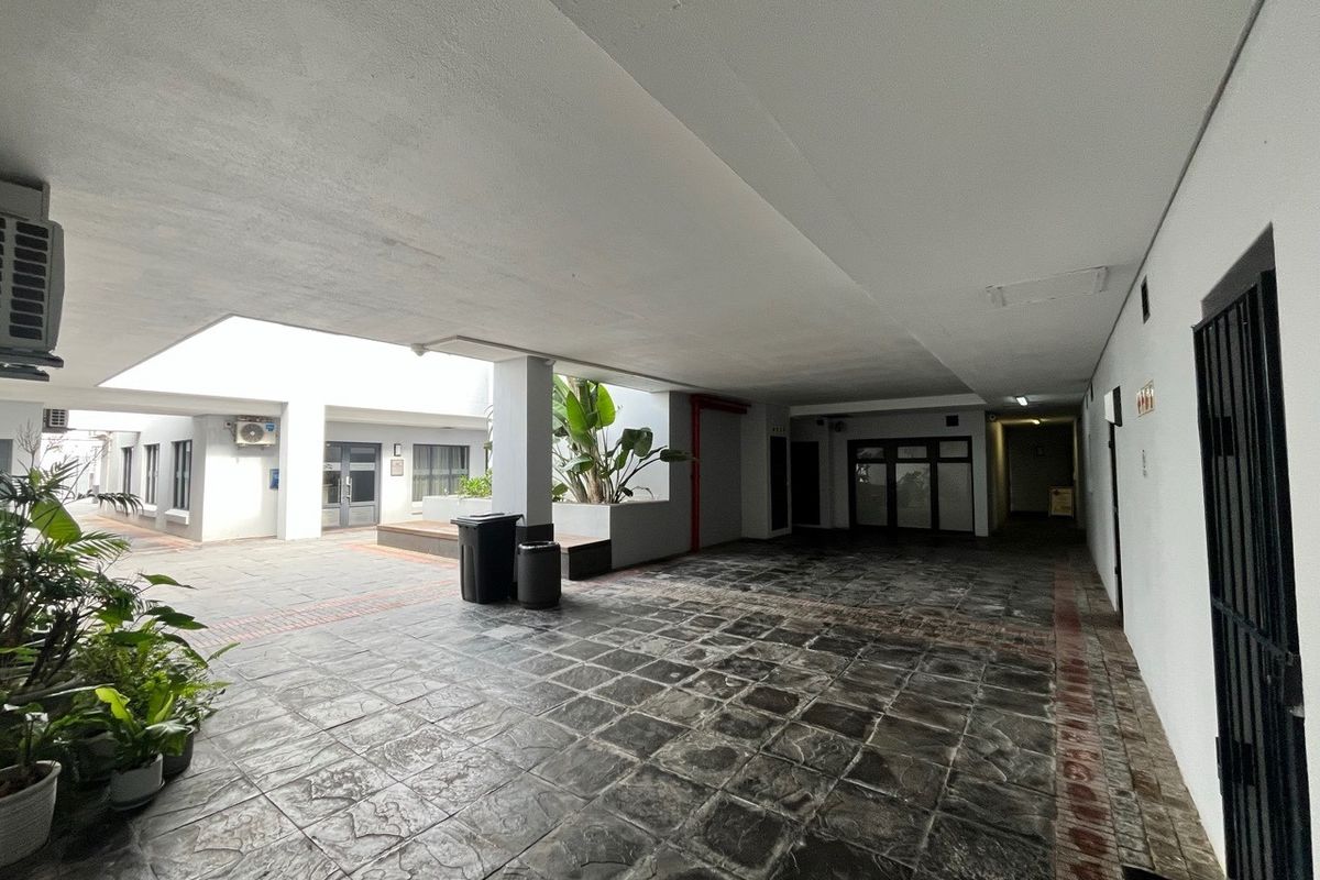 A covered outdoor patio area featuring durable tiled flooring, recessed lighting, and an integrated air conditioning unit within an office complex setting.