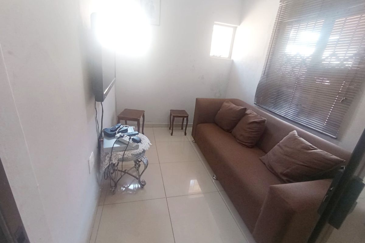 A compact living room featuring tiled flooring and venetian blinds, currently showing signs of wear on the walls.