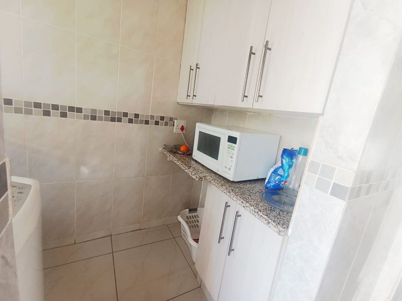 A functional laundry area featuring built-in white cabinetry, granite countertops, and tiled finishes, providing practical utility space.