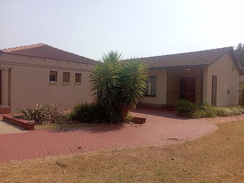 Front exterior view of a single-story house featuring a tiled roof, paved driveway, and security gate entrance.