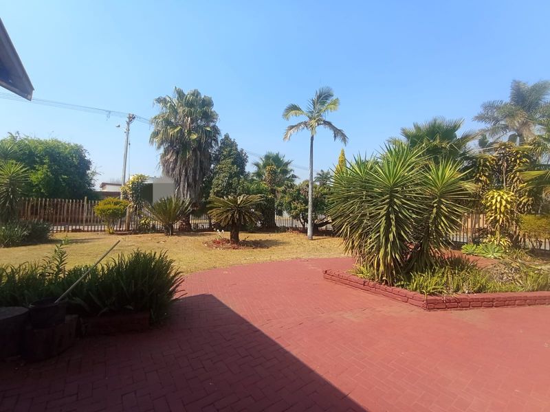 A spacious garden area featuring a red brick paved patio, established landscaping, and perimeter fencing.