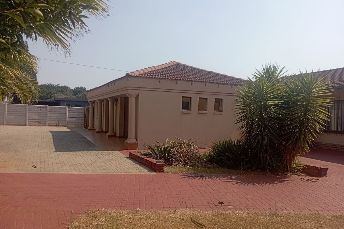 Rear view of the property featuring a paved driveway, covered patio area with columns, and a tiled roof structure.