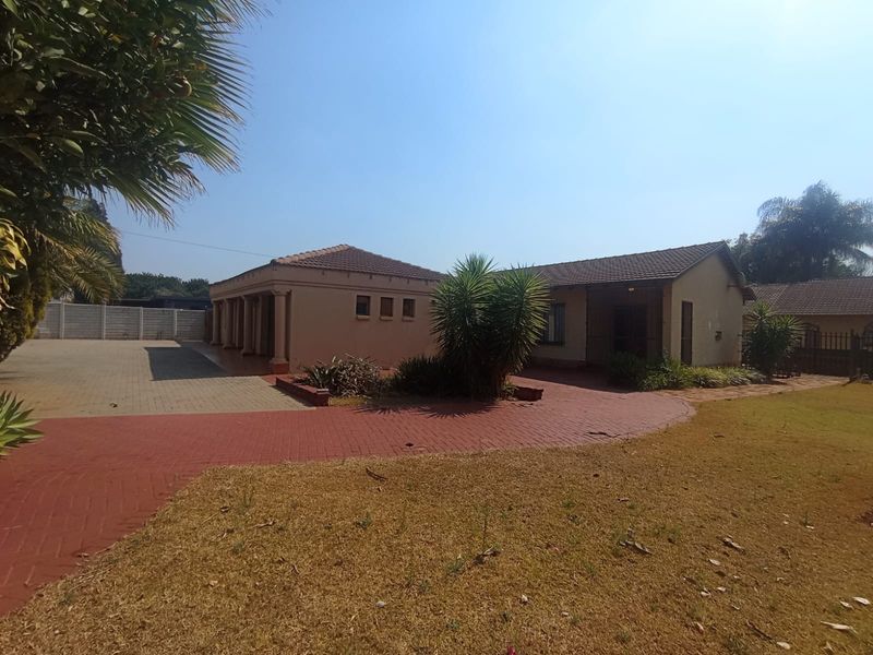 Front view of the property featuring a paved driveway, covered patio area, and established garden space with a tiled roof structure.