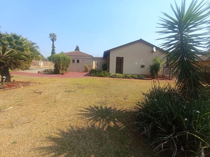 Rear view of the property featuring a large garden area, paved driveway, and exterior building facade with security gate.