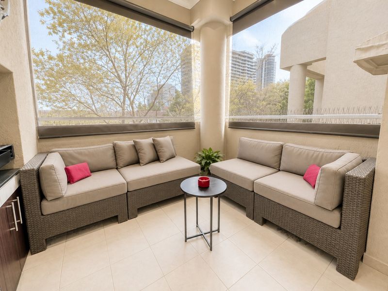 A covered balcony featuring tiled flooring, built-in cabinetry, and retractable roller blinds, providing a comfortable outdoor seating area.