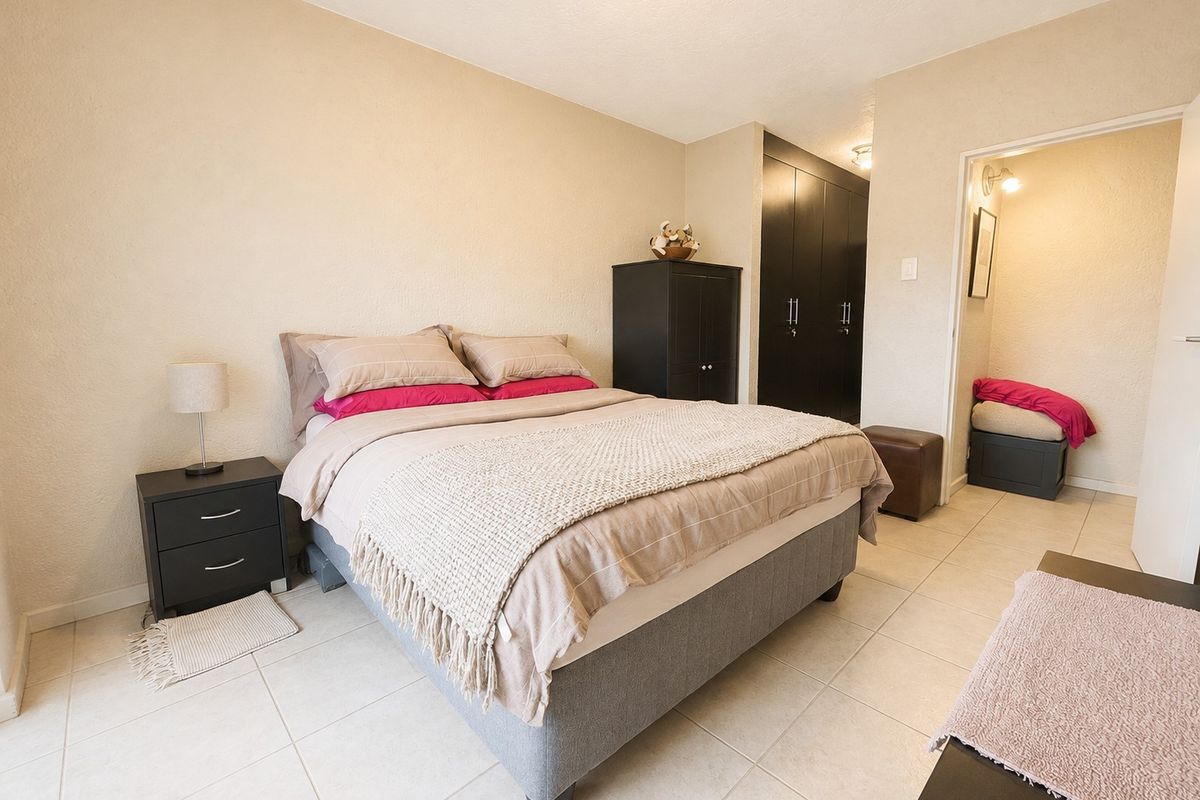 A bedroom featuring tiled flooring and built-in cupboards, with an adjoining space visible through the doorway.