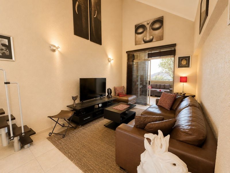 A bright living room featuring a high vaulted ceiling, tiled flooring, and a sliding glass door providing access to an outdoor balcony area.