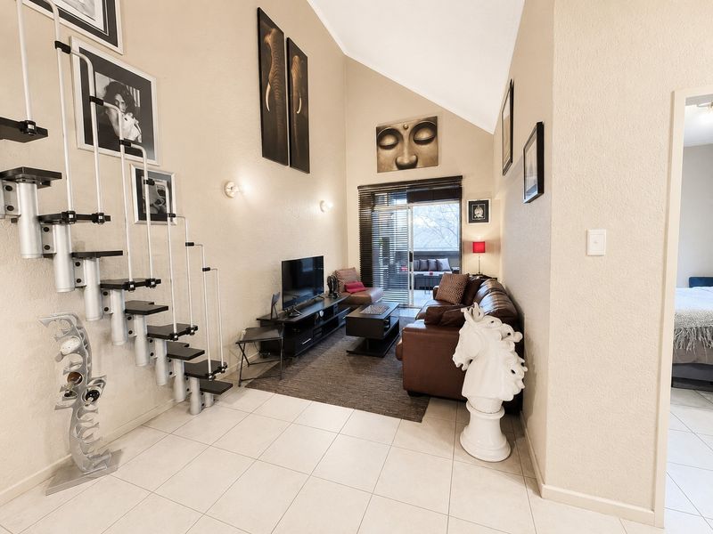 A bright living room featuring a high vaulted ceiling, tiled flooring, and a modern staircase, with direct access to an outdoor balcony area.