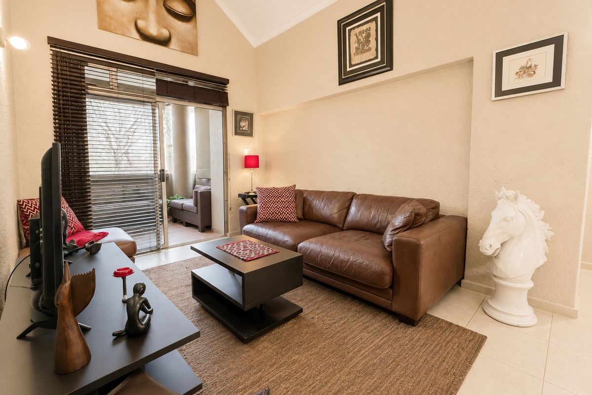 A bright living room featuring a vaulted ceiling, tiled flooring, and a sliding glass door providing access to an outdoor balcony area.