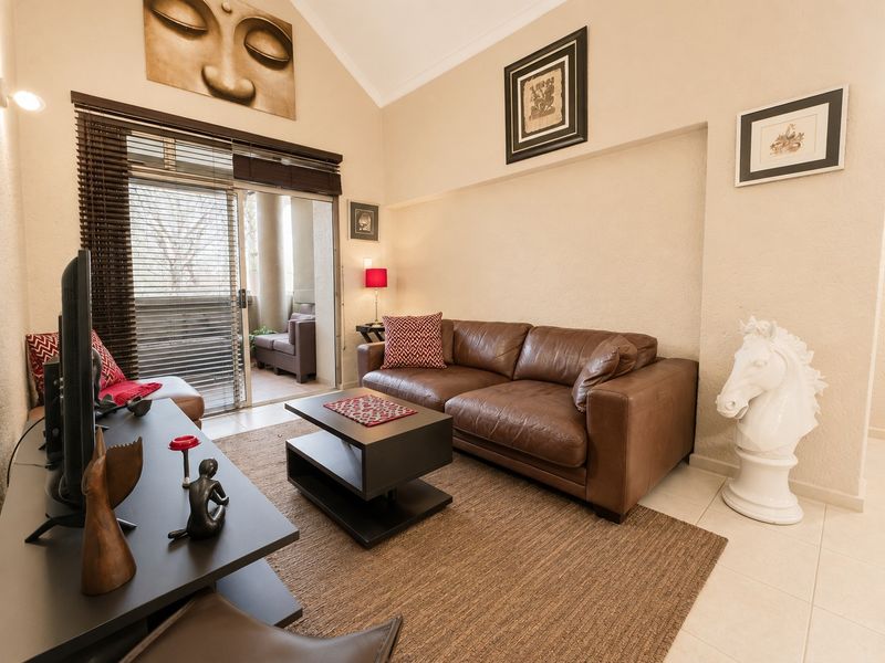 A bright living room featuring a vaulted ceiling, tiled flooring, and a sliding glass door providing access to an outdoor balcony area.