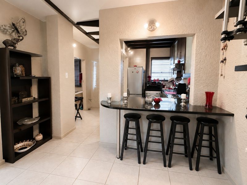 Open plan living area featuring a breakfast bar with granite countertop, connecting to a functional kitchen with built-in cabinetry and tiled flooring throughout.