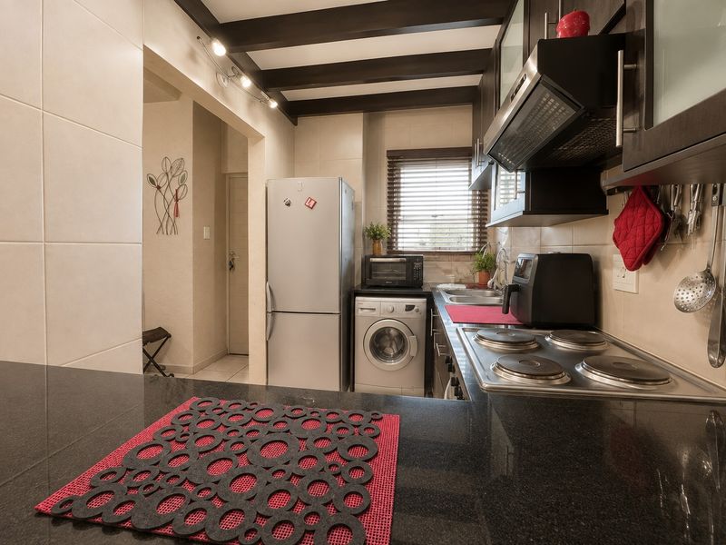 Compact kitchen featuring dark cabinetry, granite countertops, an electric hob with extractor fan, and exposed ceiling beams, providing a functional and well-maintained cooking space.